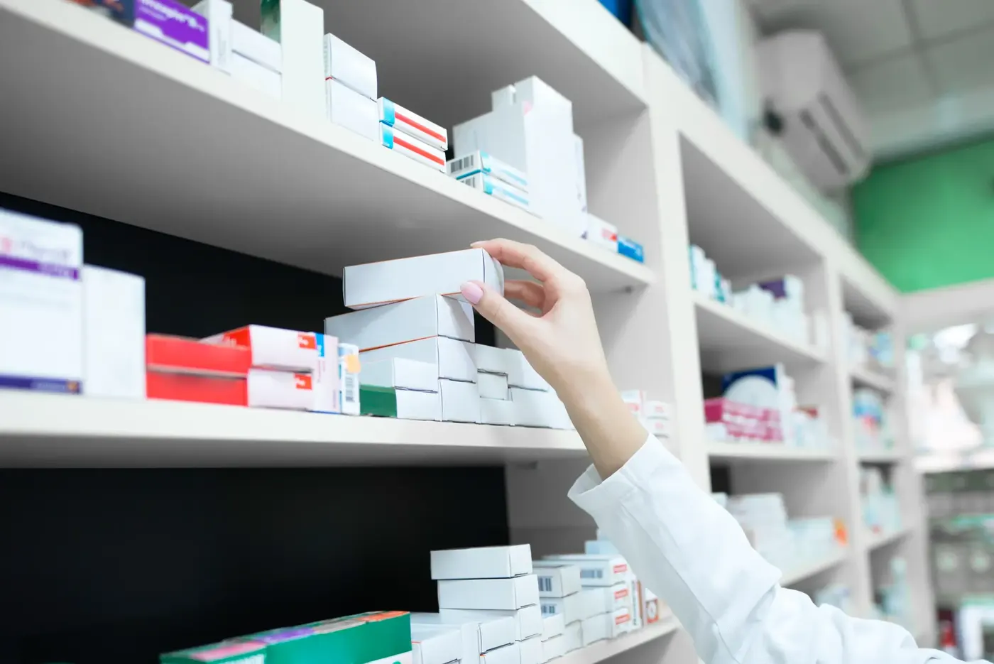 Une pharmacienne prend une boîte de médicament dans les rayons de l'officine.